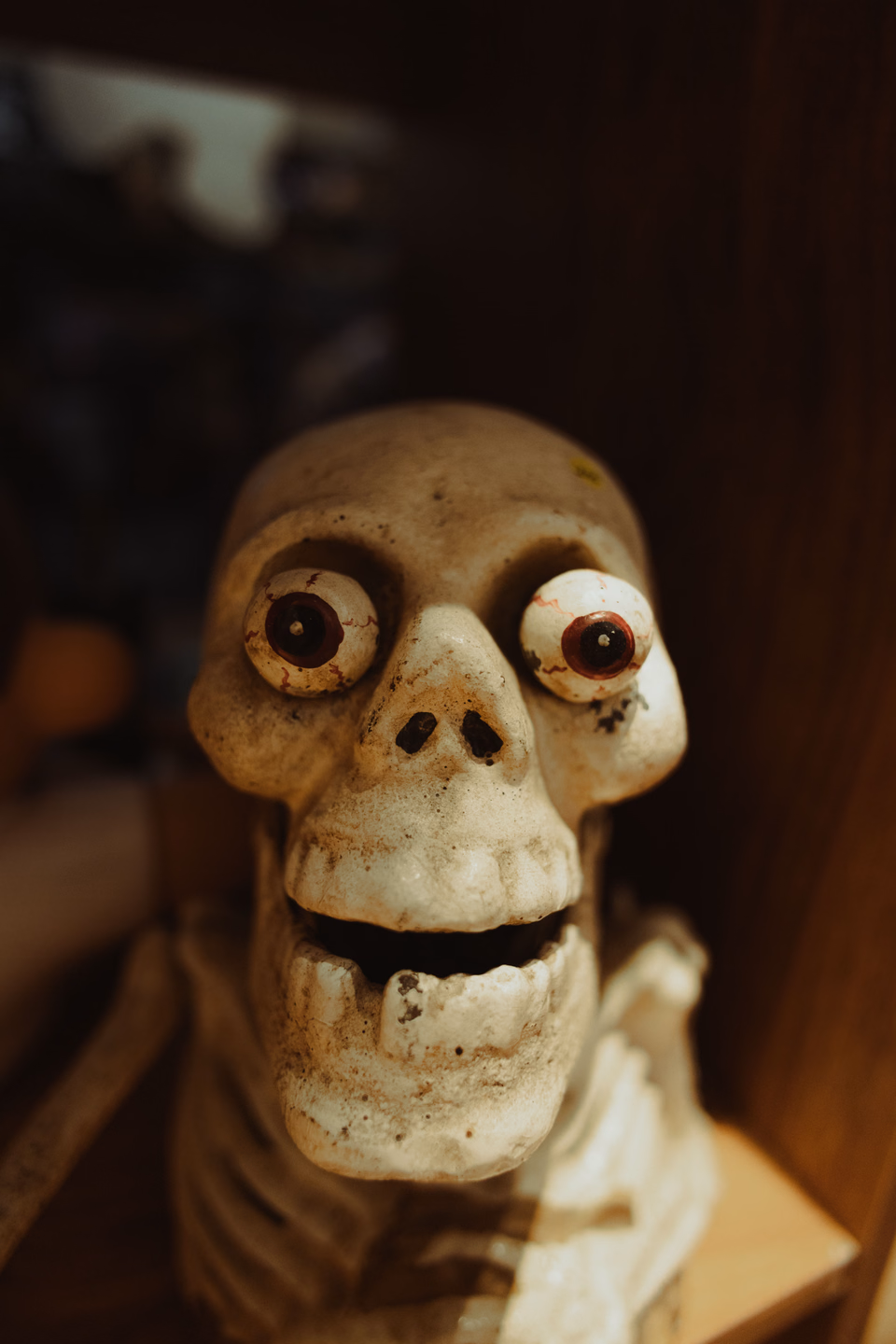 Close-up of a skeleton decoration with bulging round eyes and a toothy grin, lit warm against a dark background