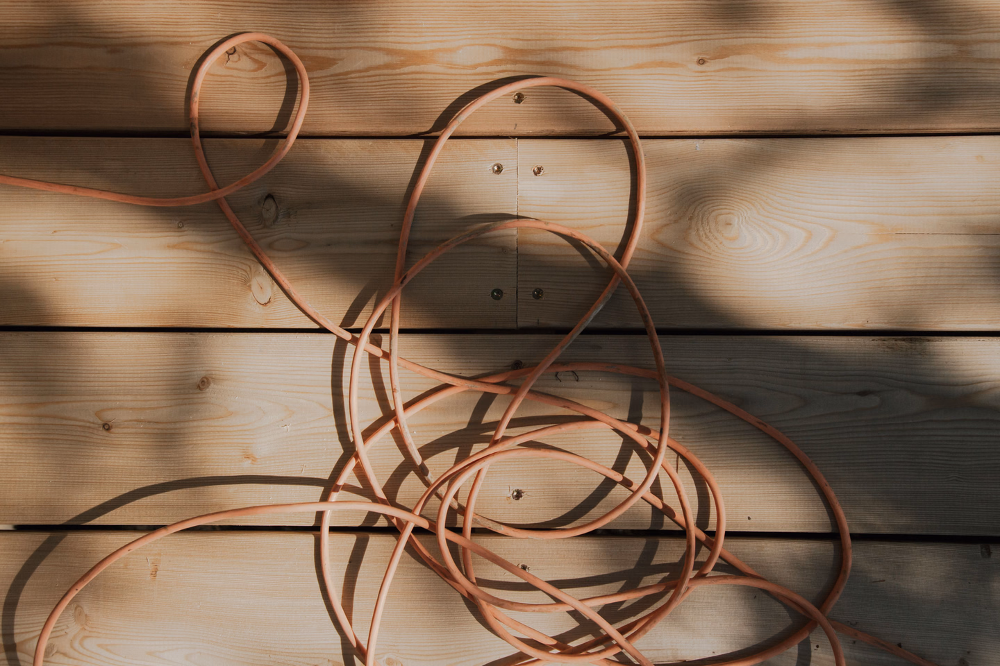 An orange extension cord coiled loosely across sunlit wooden planks