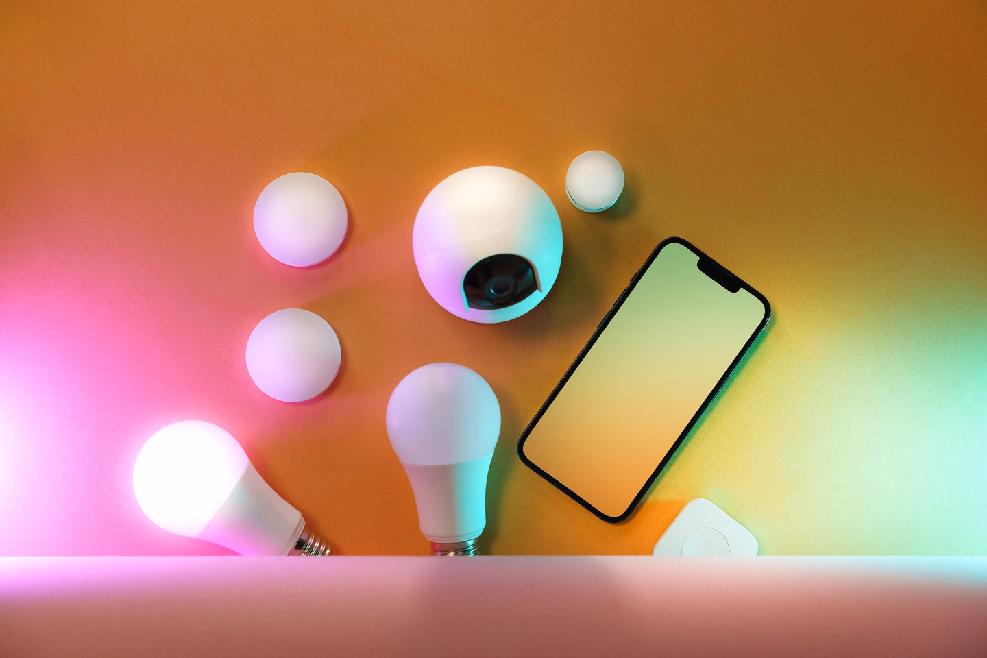 A smartphone lying among smart bulbs and small smart home devices on a table