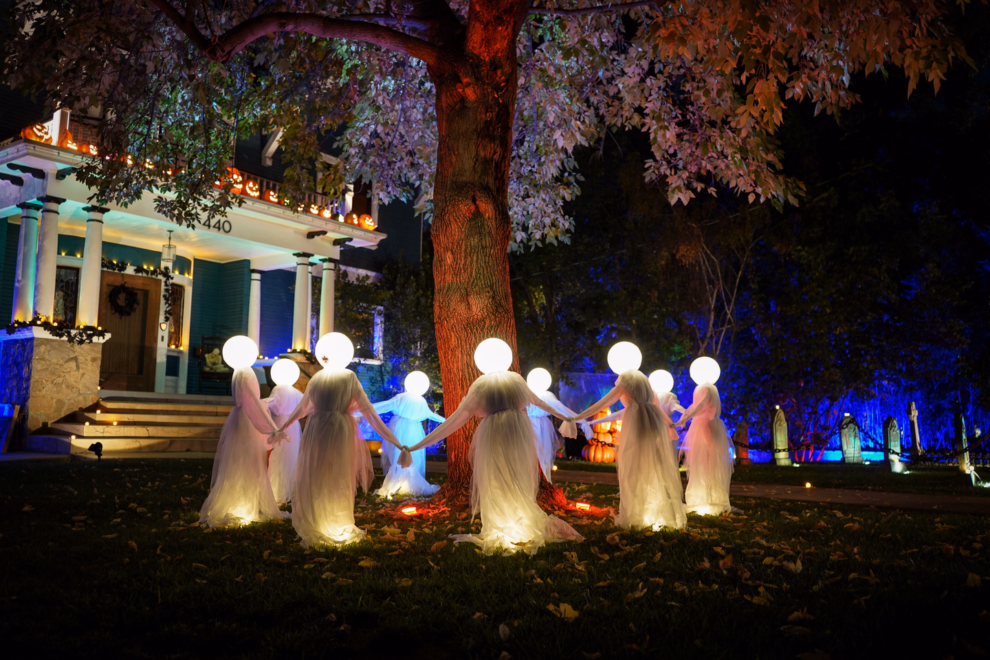 Glowing ghost figures hanging from a tree over a dark suburban lawn at night