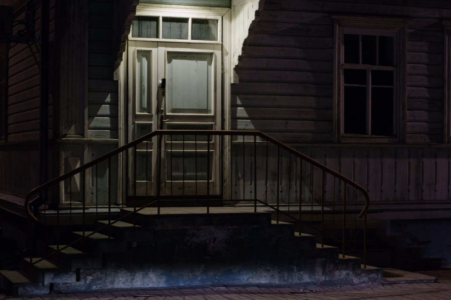 A dim wooden porch and front door at night, the steps and railing barely lit
