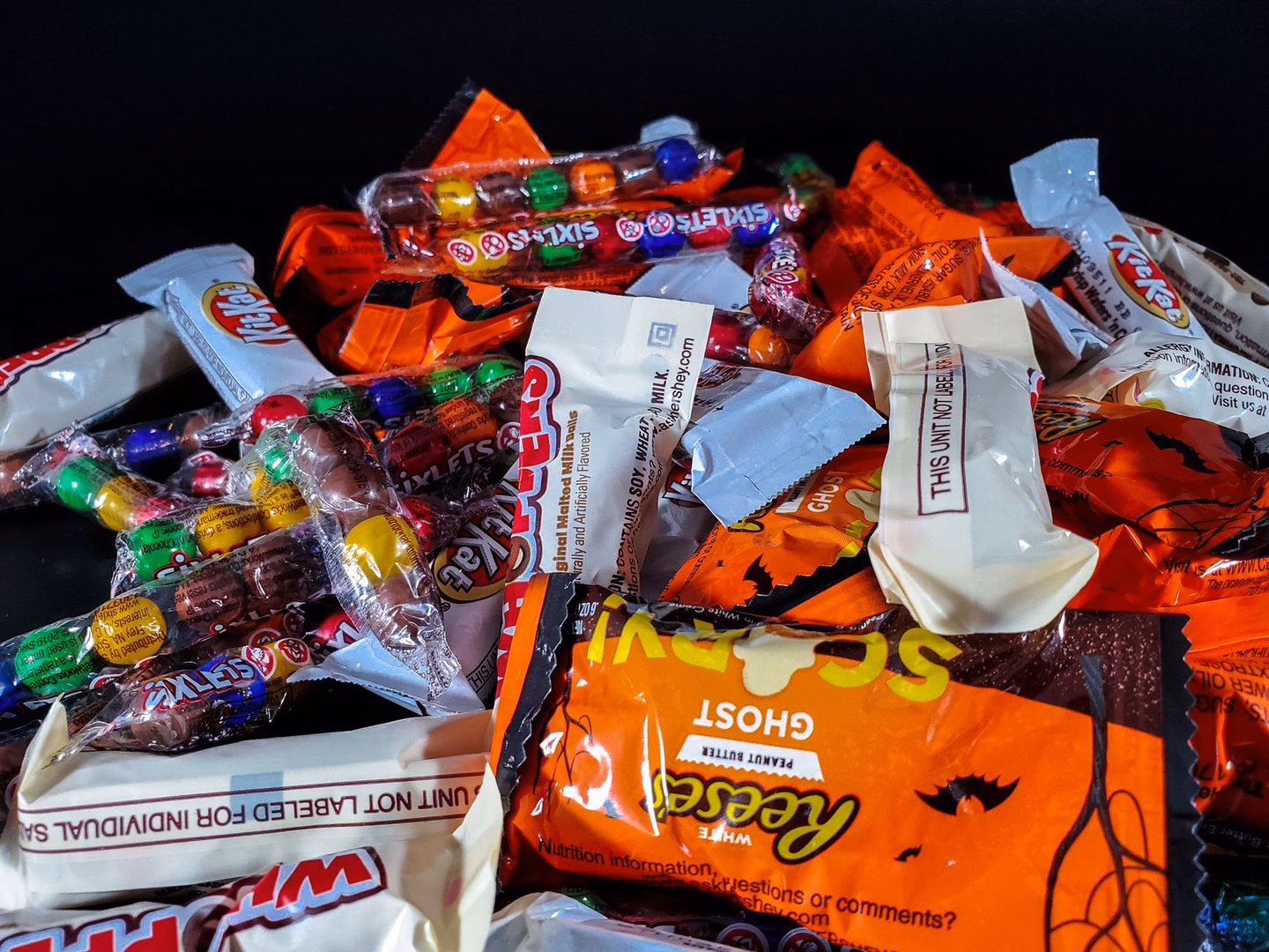 A pile of wrapped fun-size Halloween candy, including Reese's ghosts, Kit Kats and tubes of candy-coated chocolate