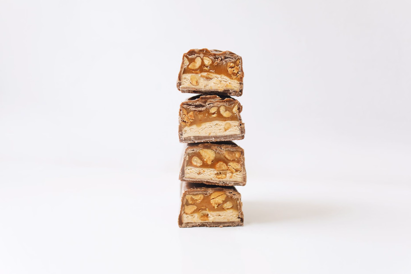 Four halves of a caramel and peanut chocolate bar stacked on a white table