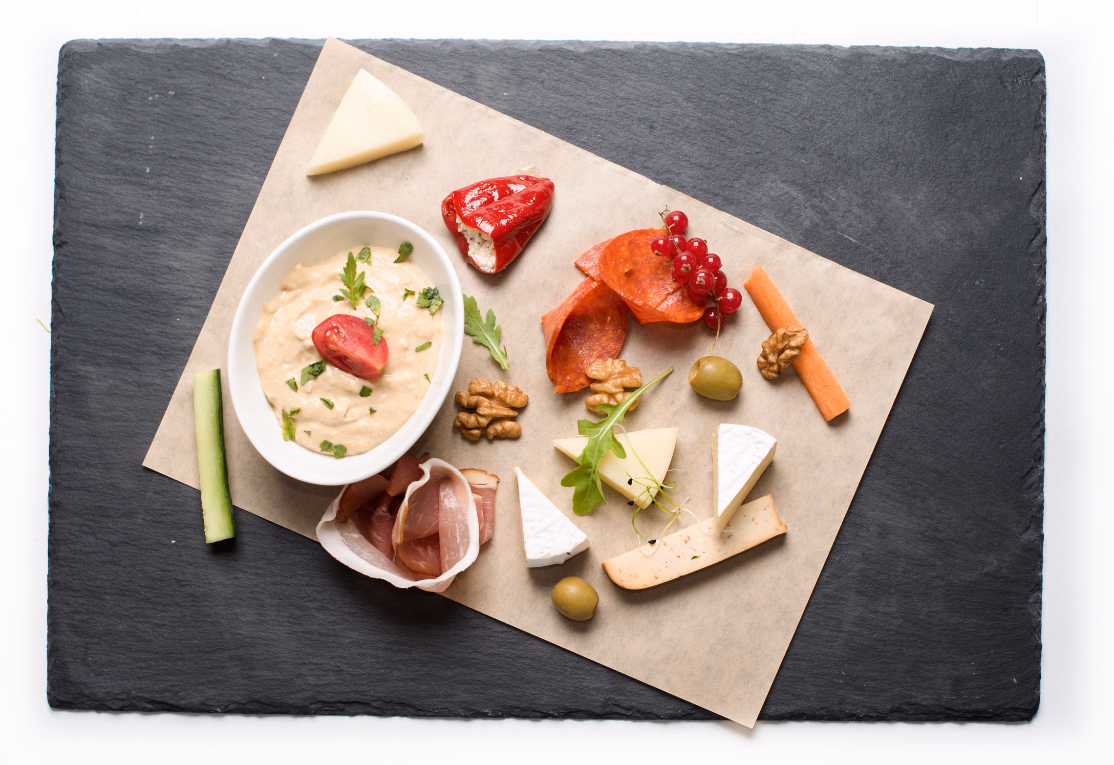 A dark slate serving board arranged with cheeses, cured meats, and garnish