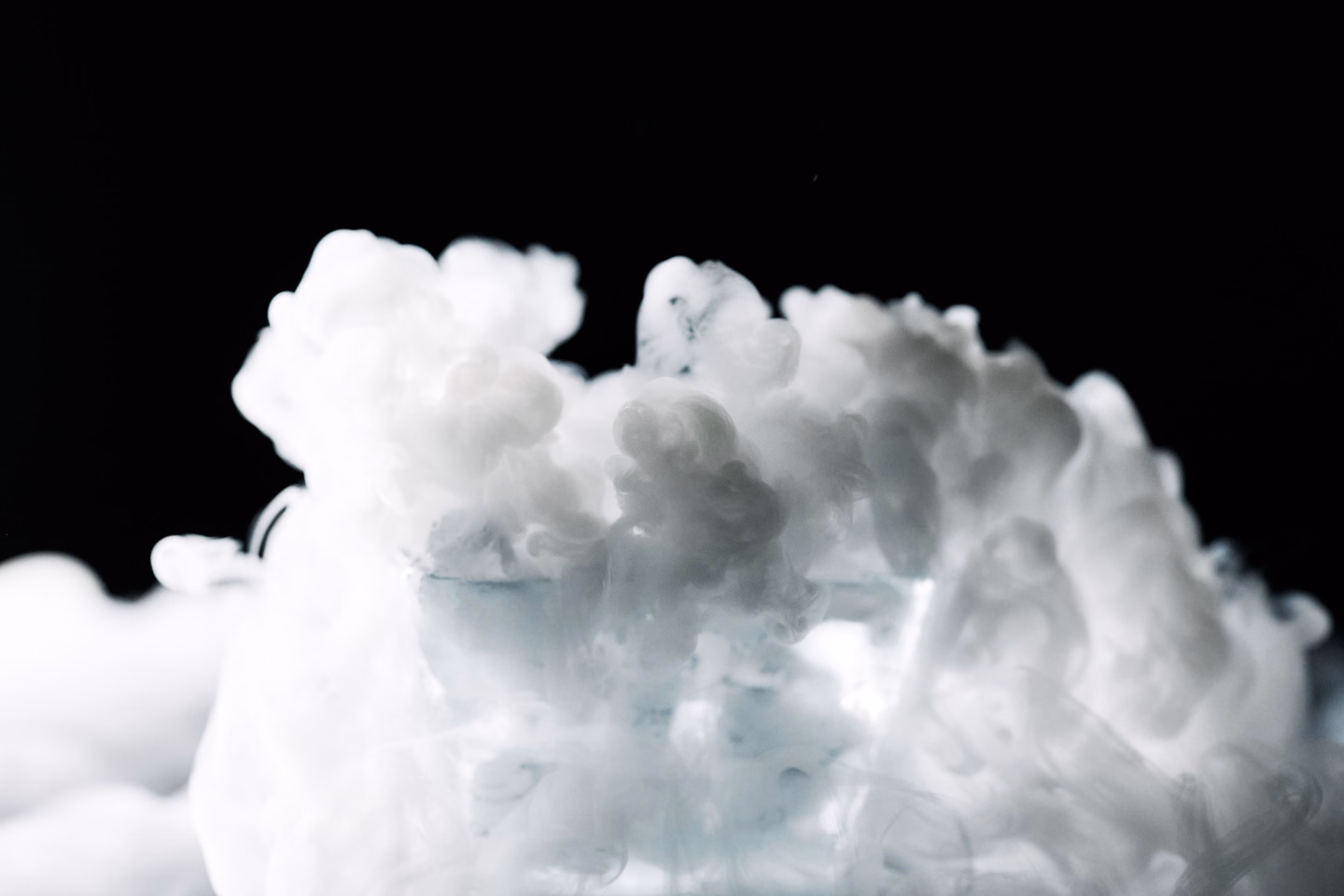 A dense white cloud of dry ice fog billowing upward against a black background