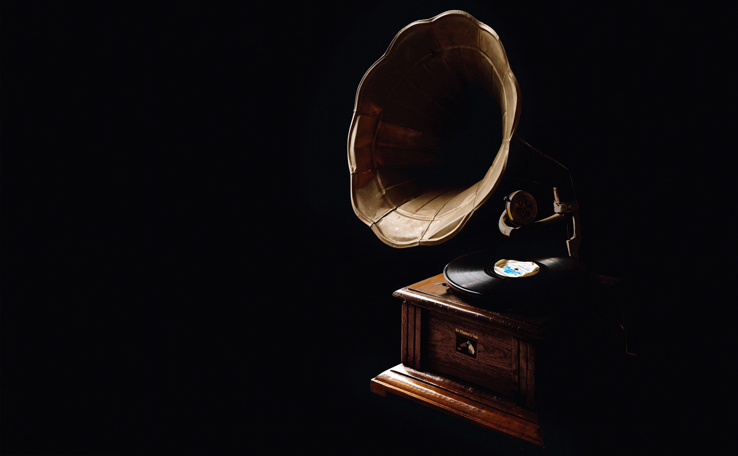 An antique gramophone with a brass horn and a wooden cabinet, lit from one side against a black background