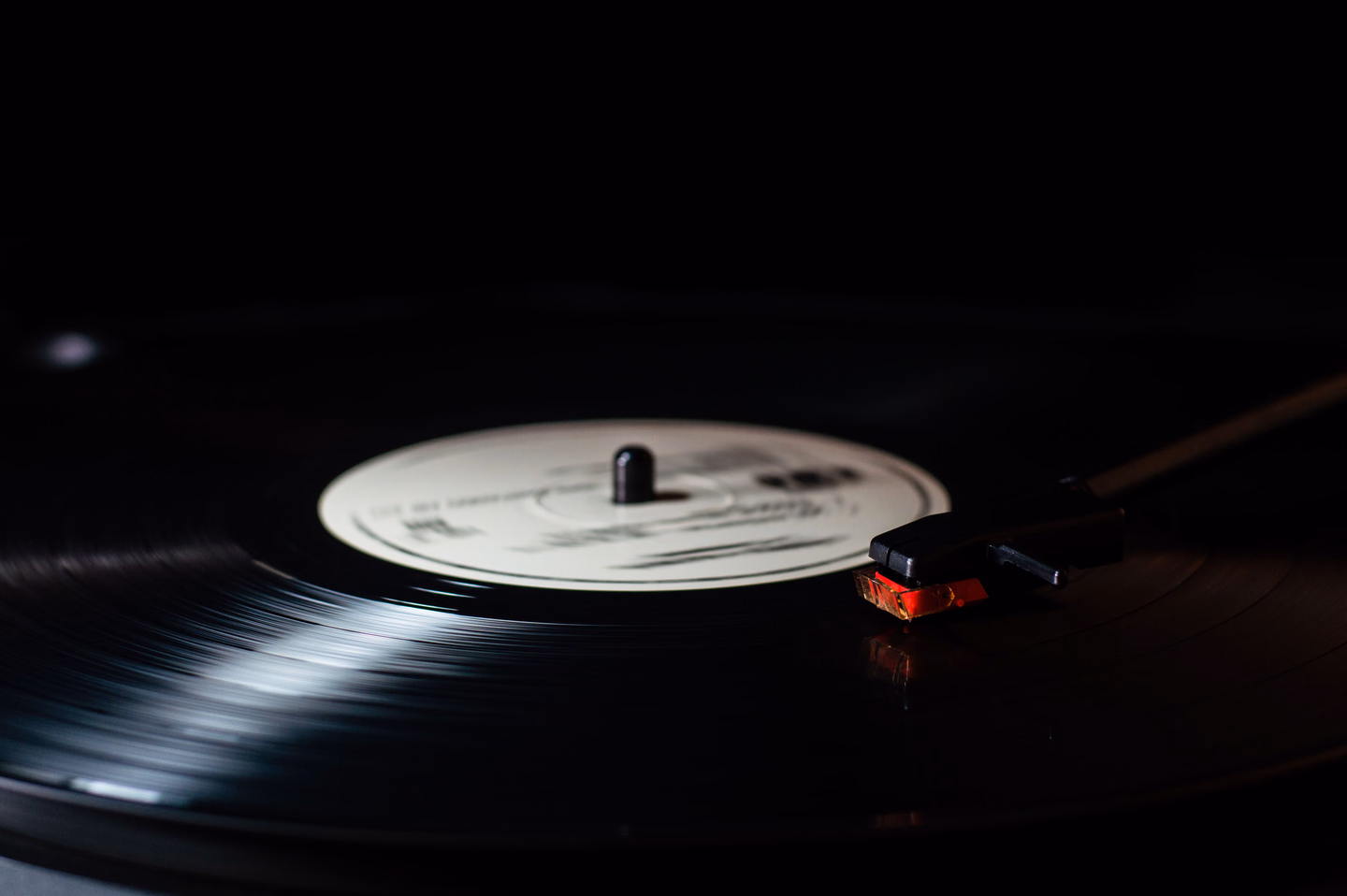 A black vinyl record with a plain white label spinning on a turntable in low light, the tonearm resting in the groove
