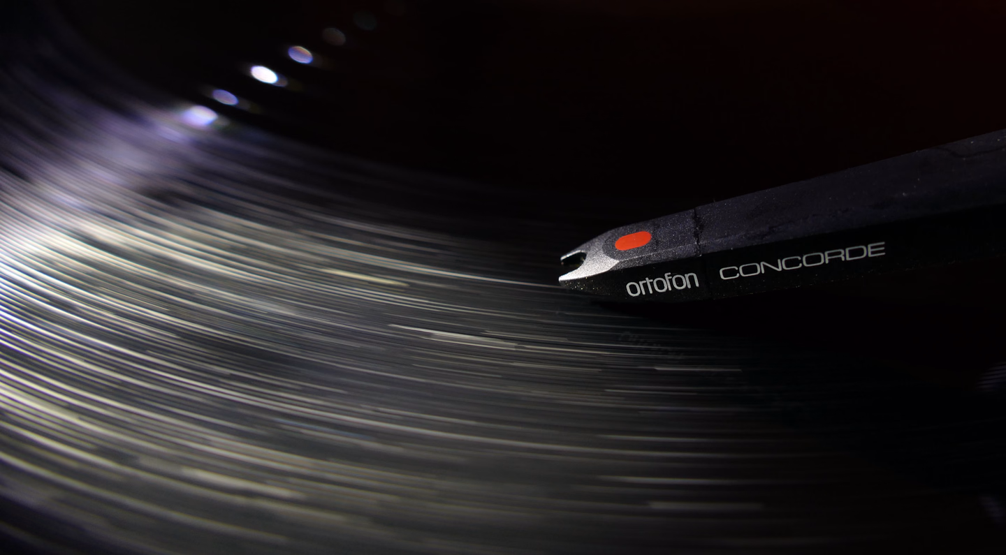 Close-up of a cartridge and stylus riding the grooves of a spinning black record, the grooves blurred into streaks of light