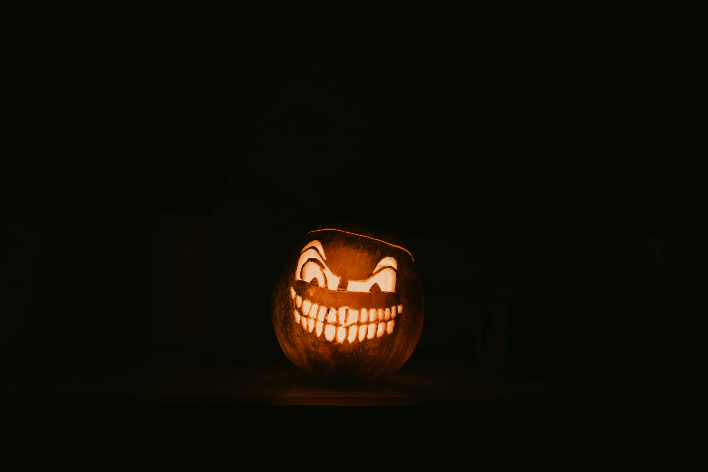 A single jack-o'-lantern with slanted eyes and a wide toothy grin glowing orange in a completely dark room