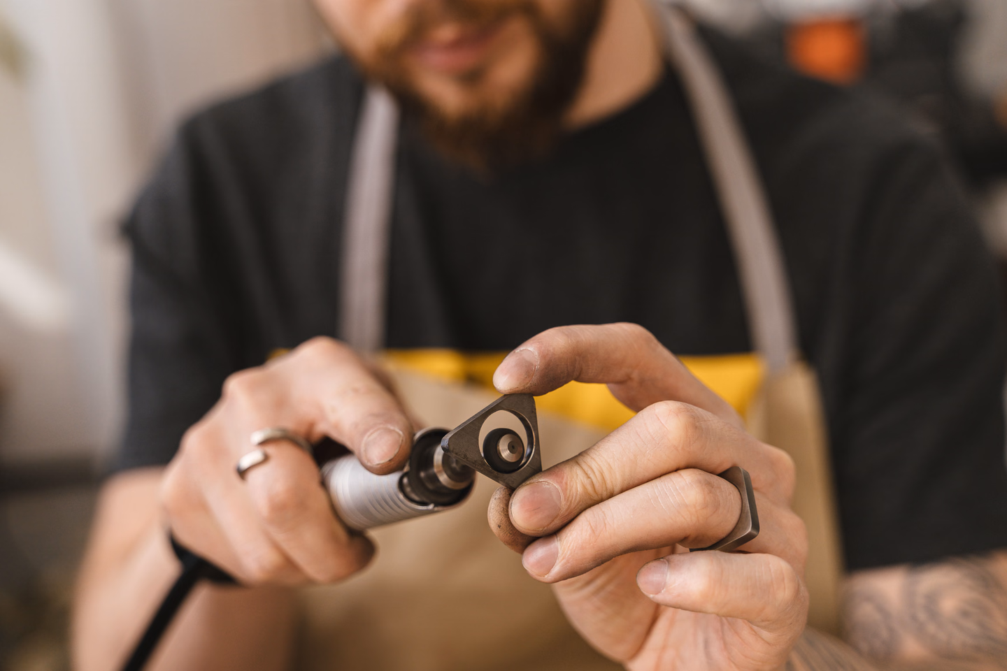 A craftsman in a work apron holding a small handheld rotary tool up close, fitting a piece to its tip