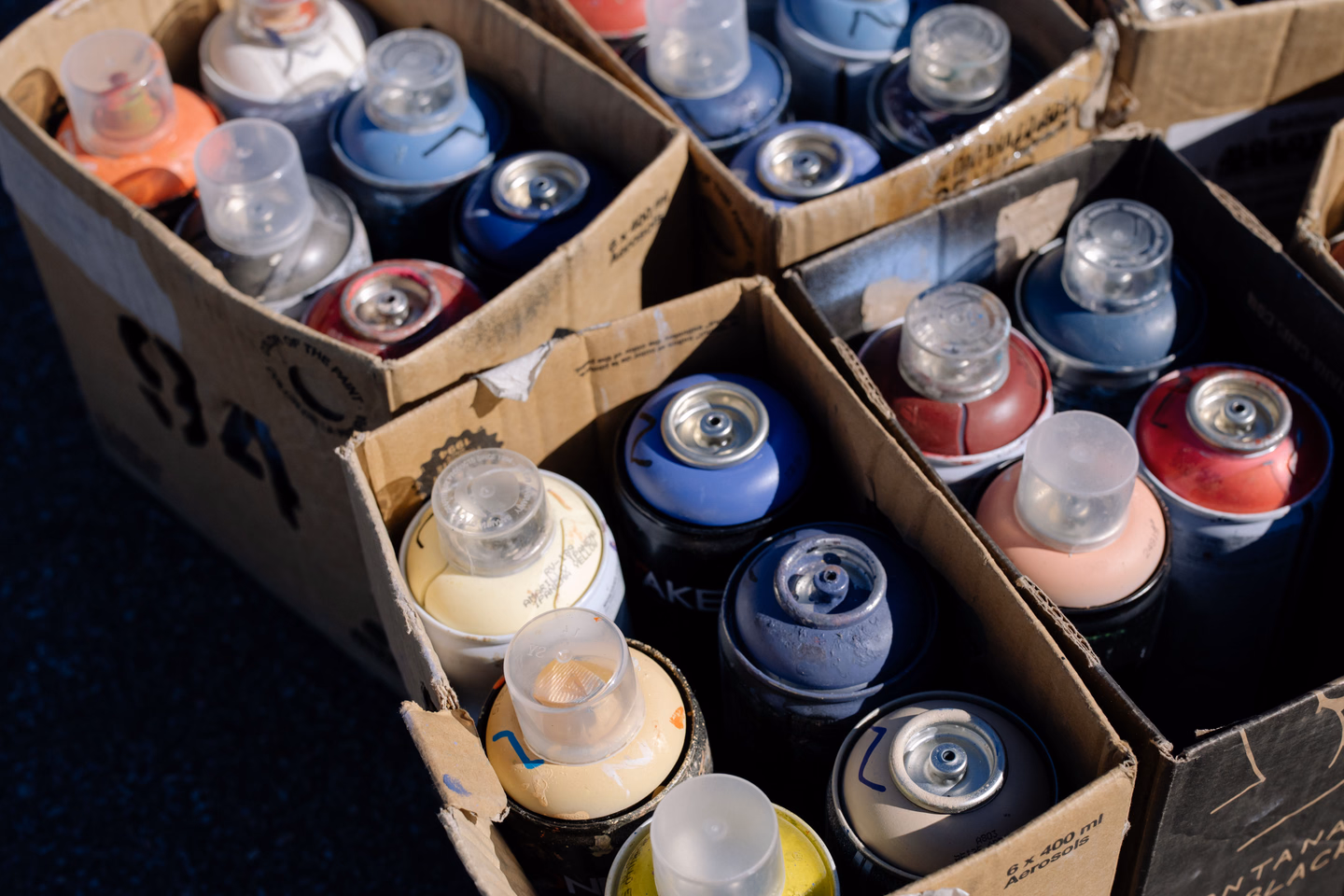 Rows of aerosol spray paint cans with clear caps standing in cardboard boxes