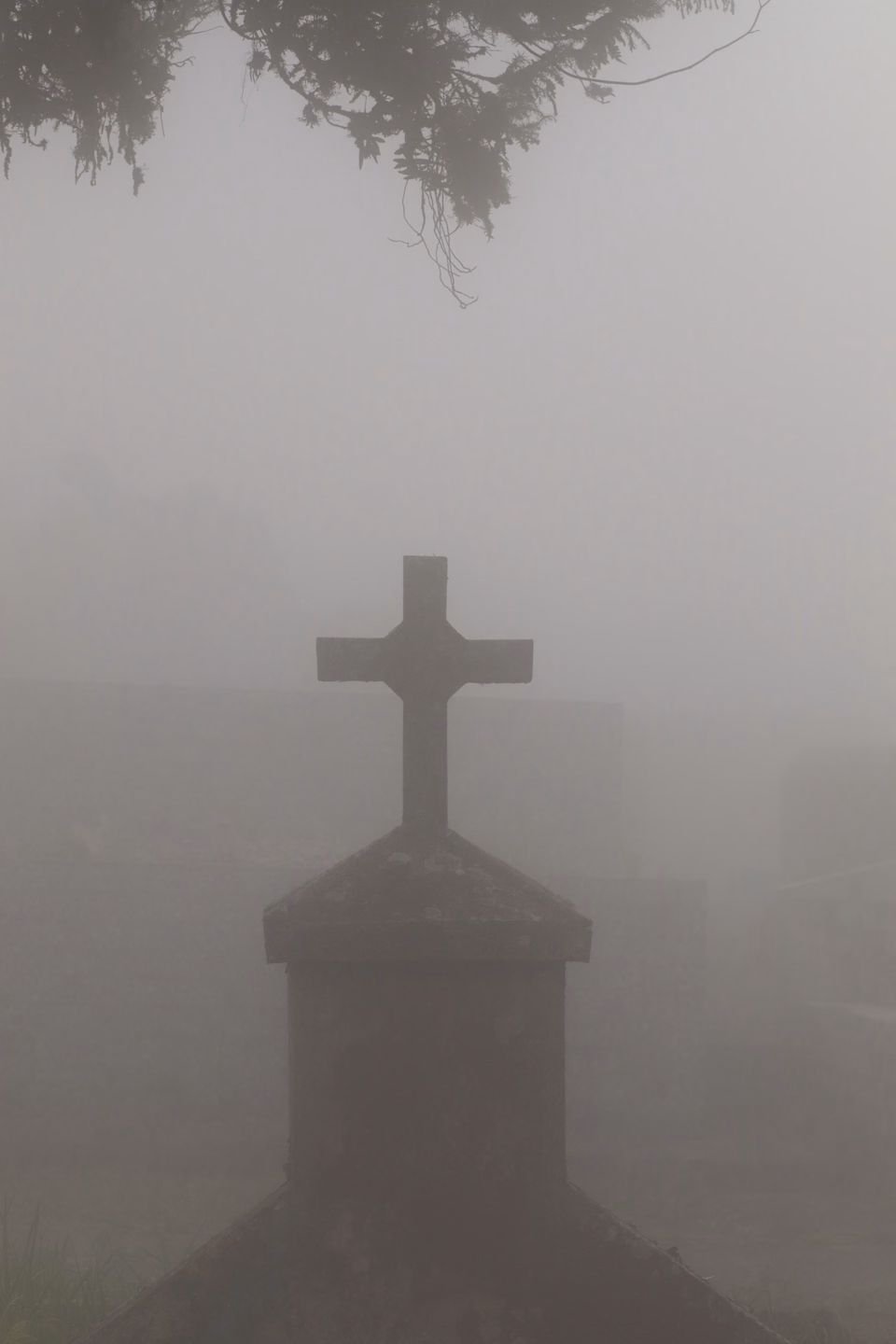 A stone cross grave marker reduced to a dark silhouette in thick gray fog