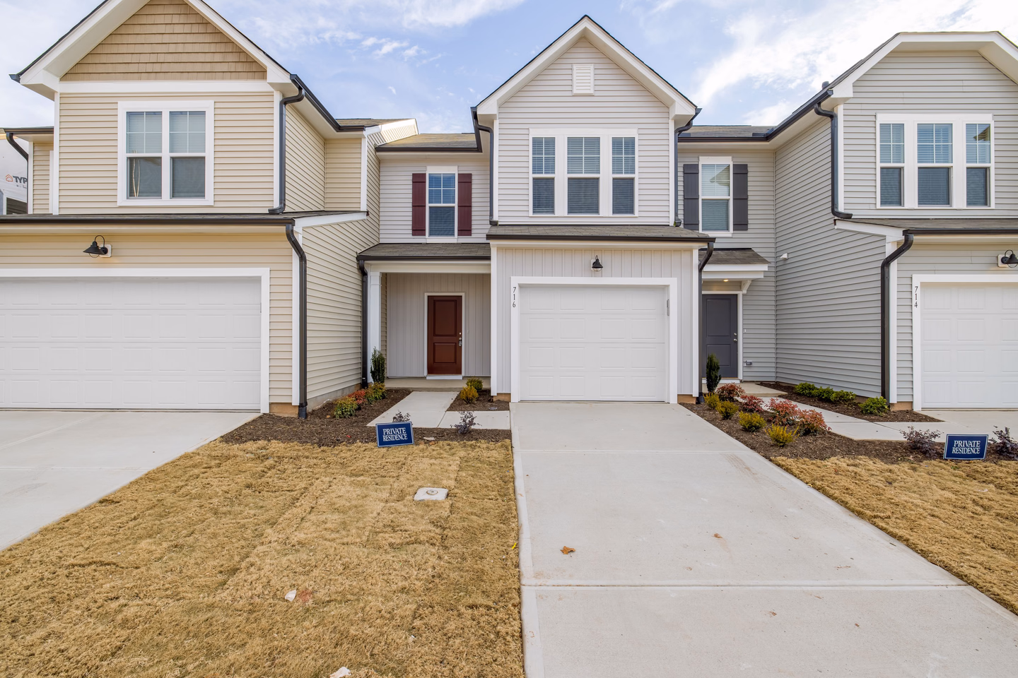 A row of new beige and gray townhouses with matching garage doors, short driveways and small lawns, a private property sign in each yard