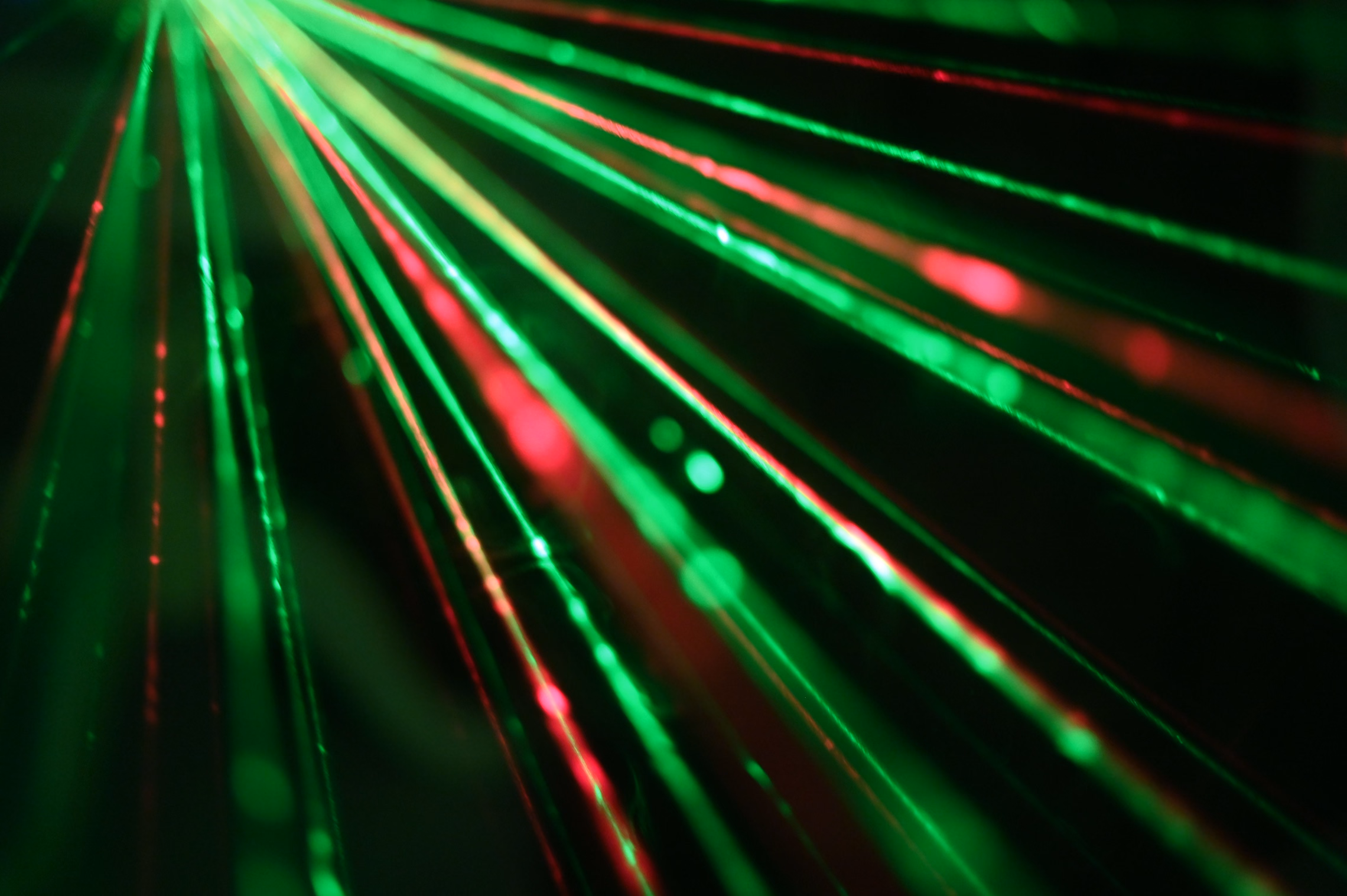Dozens of thin green and red laser beams fanning out from one point through a dark, hazy room