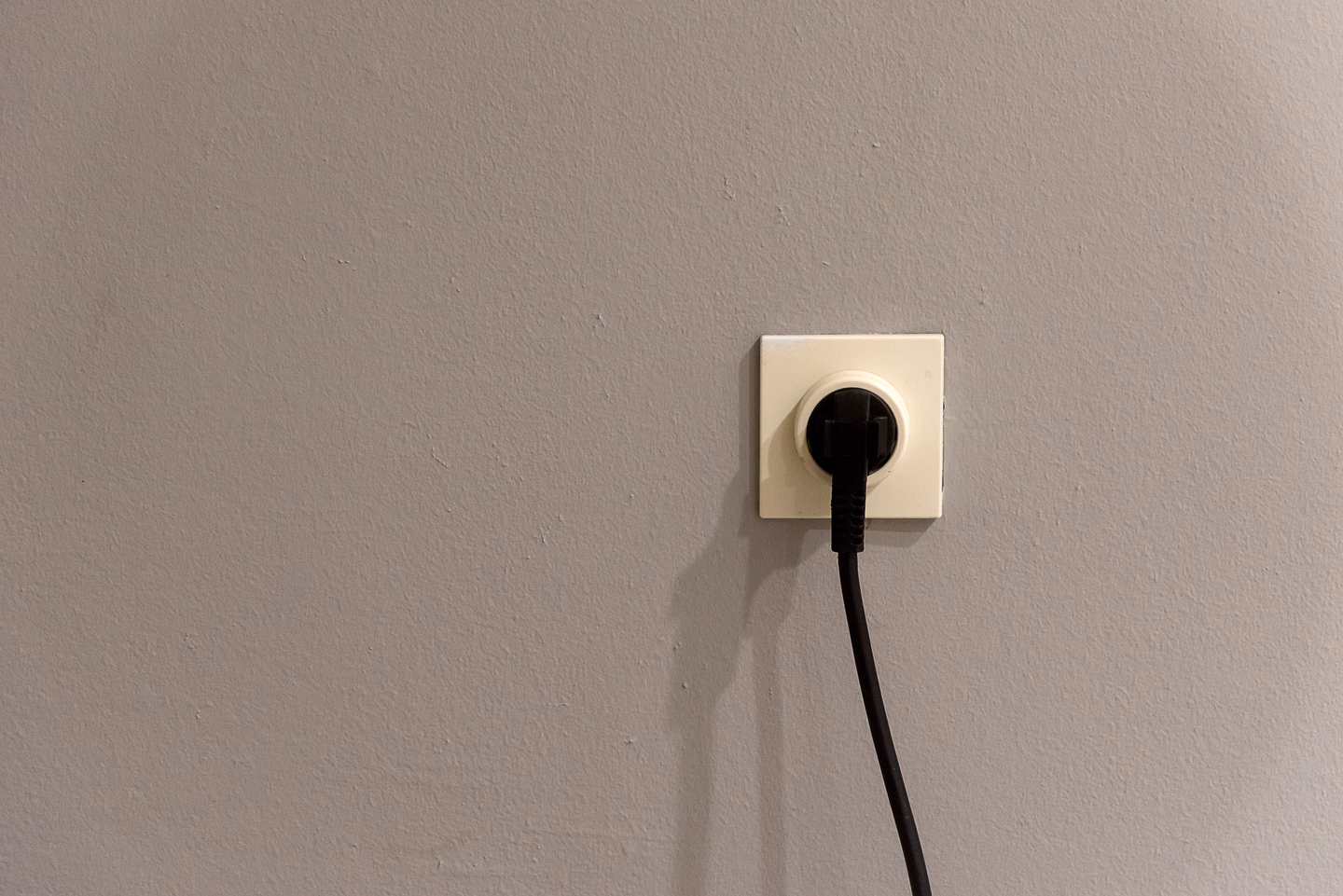 A black plug pushed into a white socket on a plain gray wall