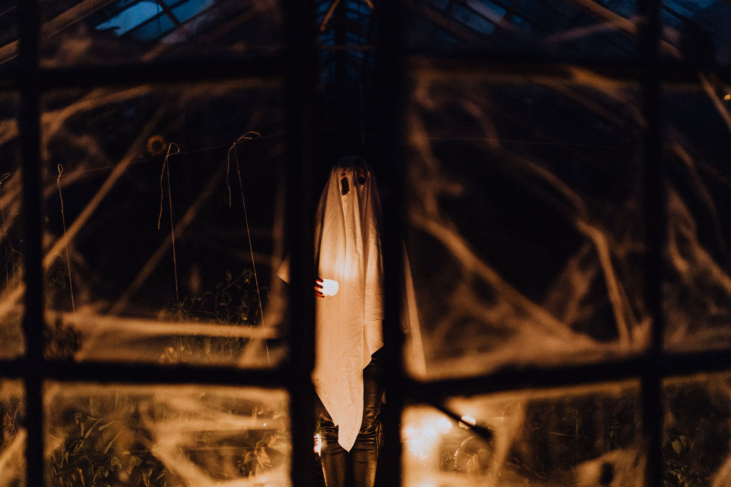 A pale sheet hanging behind a window in a dark room, lit so it looks like a standing figure