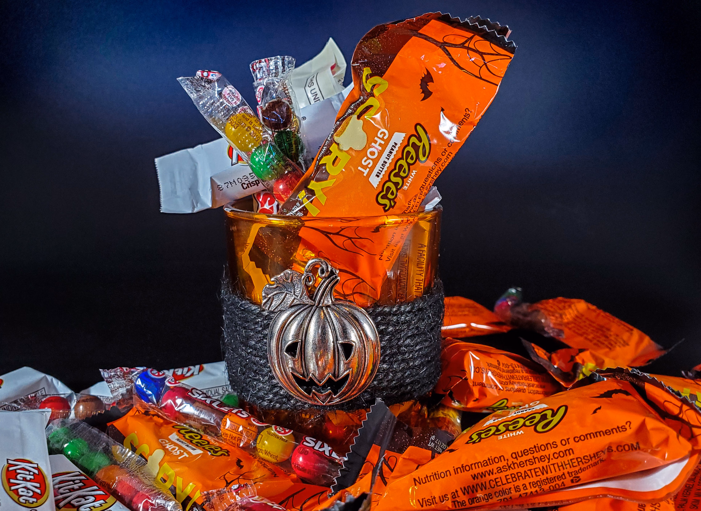 A glass bowl full of assorted wrapped Halloween candy beside a small pumpkin
