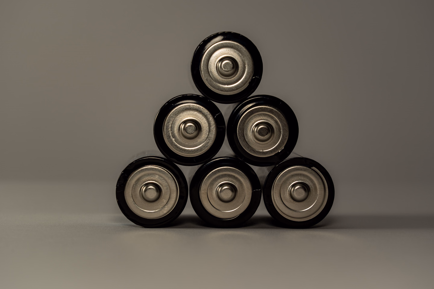 Six cylindrical batteries stacked on their sides in a small pyramid against a plain gray background, their silver ends facing the camera