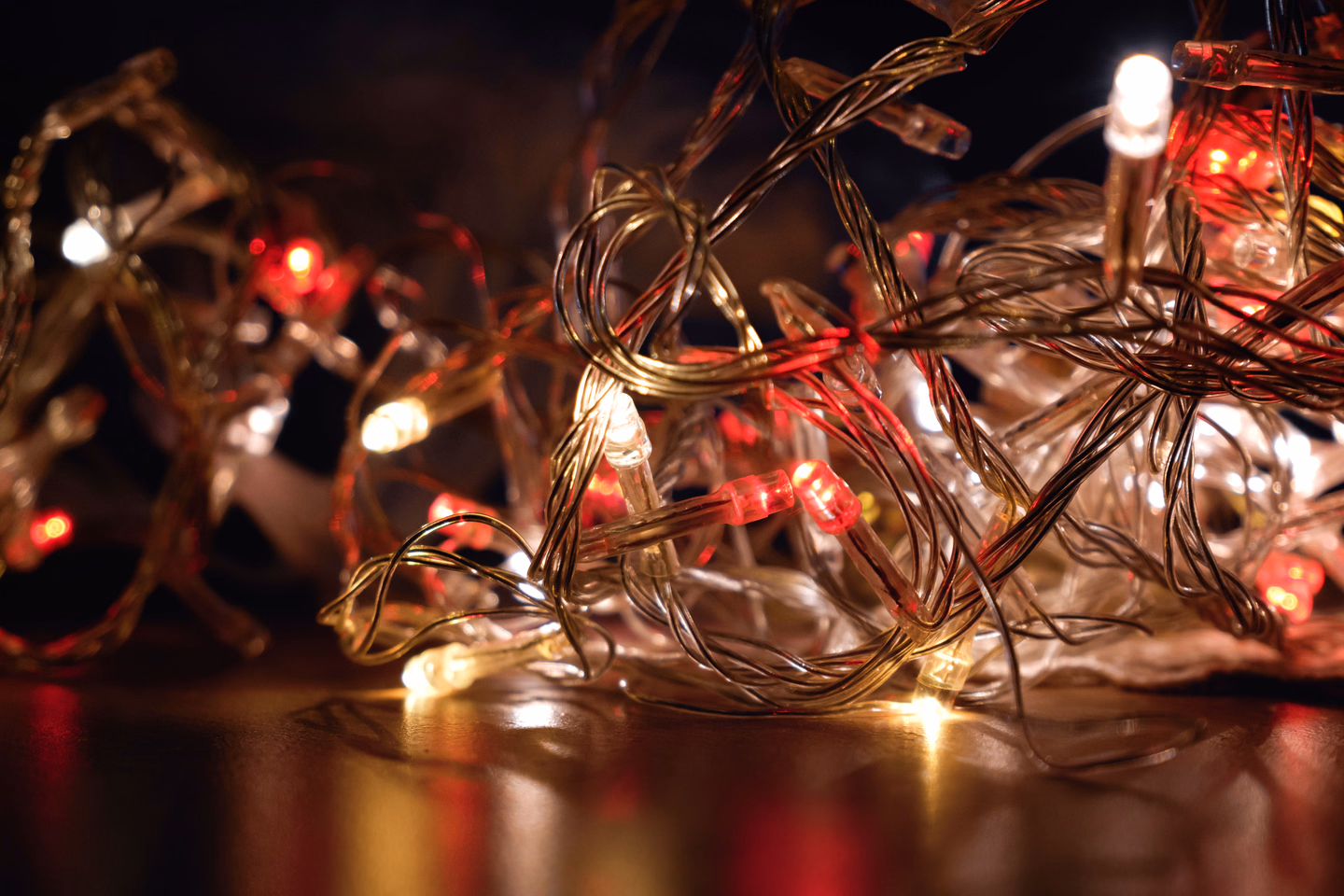 A tangled heap of clear-wire string lights glowing red, amber and white on a dark reflective surface