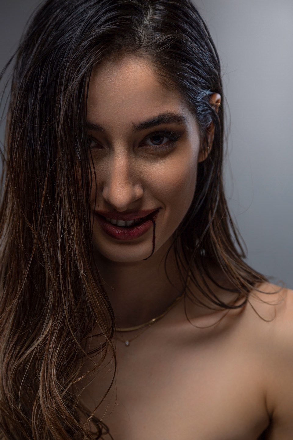 Smiling woman with dark red lips and a single thin line of fake blood running from the corner of her mouth down her chin