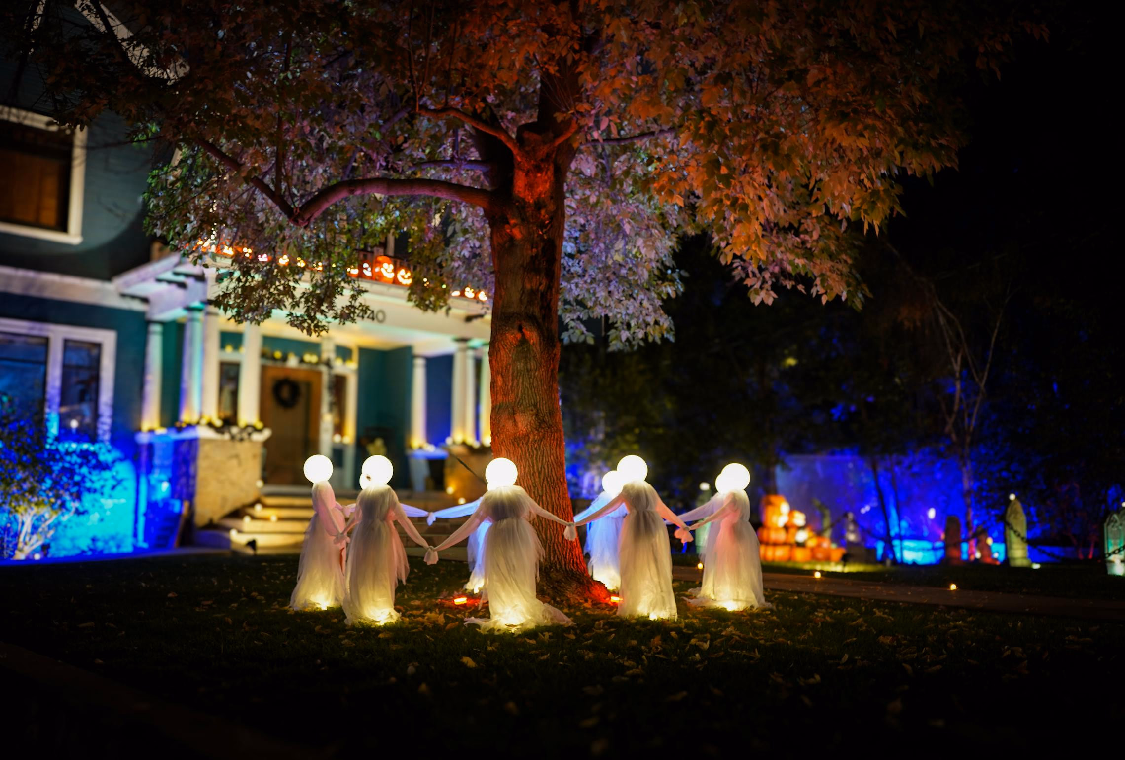 Halloween-decorated front yard at dusk with pathway lanterns, fog, and silhouetted trees