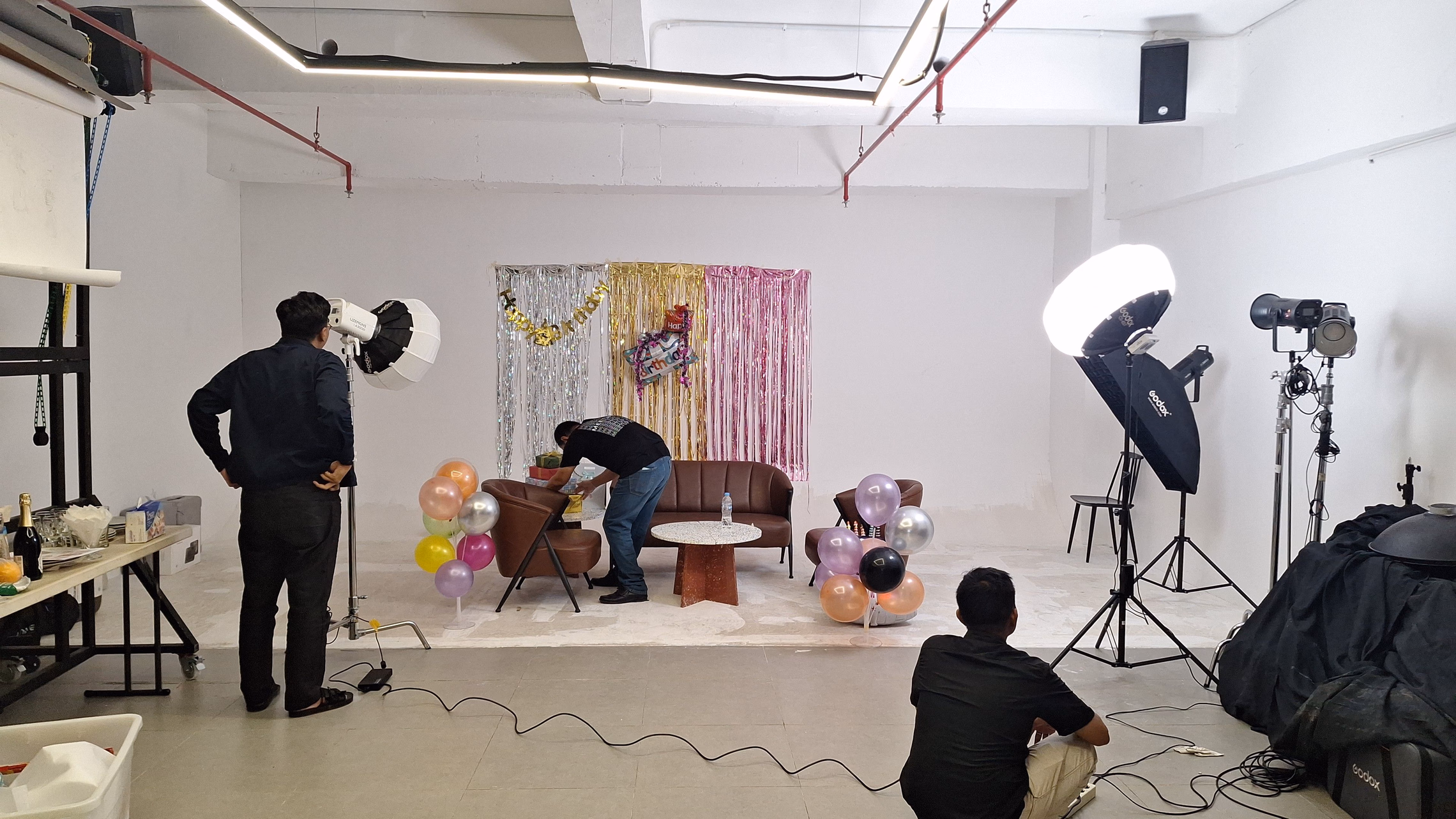 A photo booth set up in a corner with a backdrop, lighting stand, and party decorations