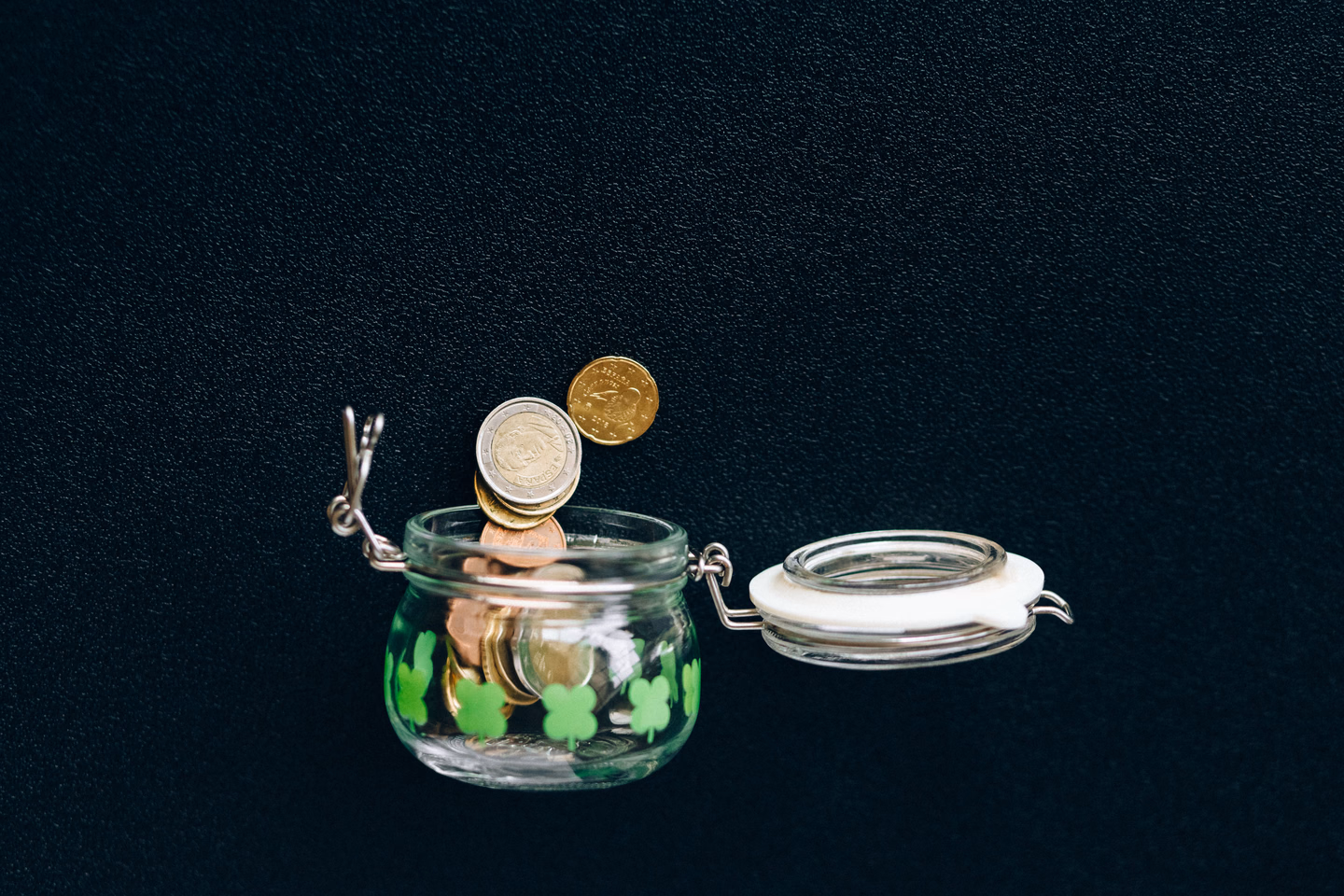 Coins falling into a glass jar against a black background