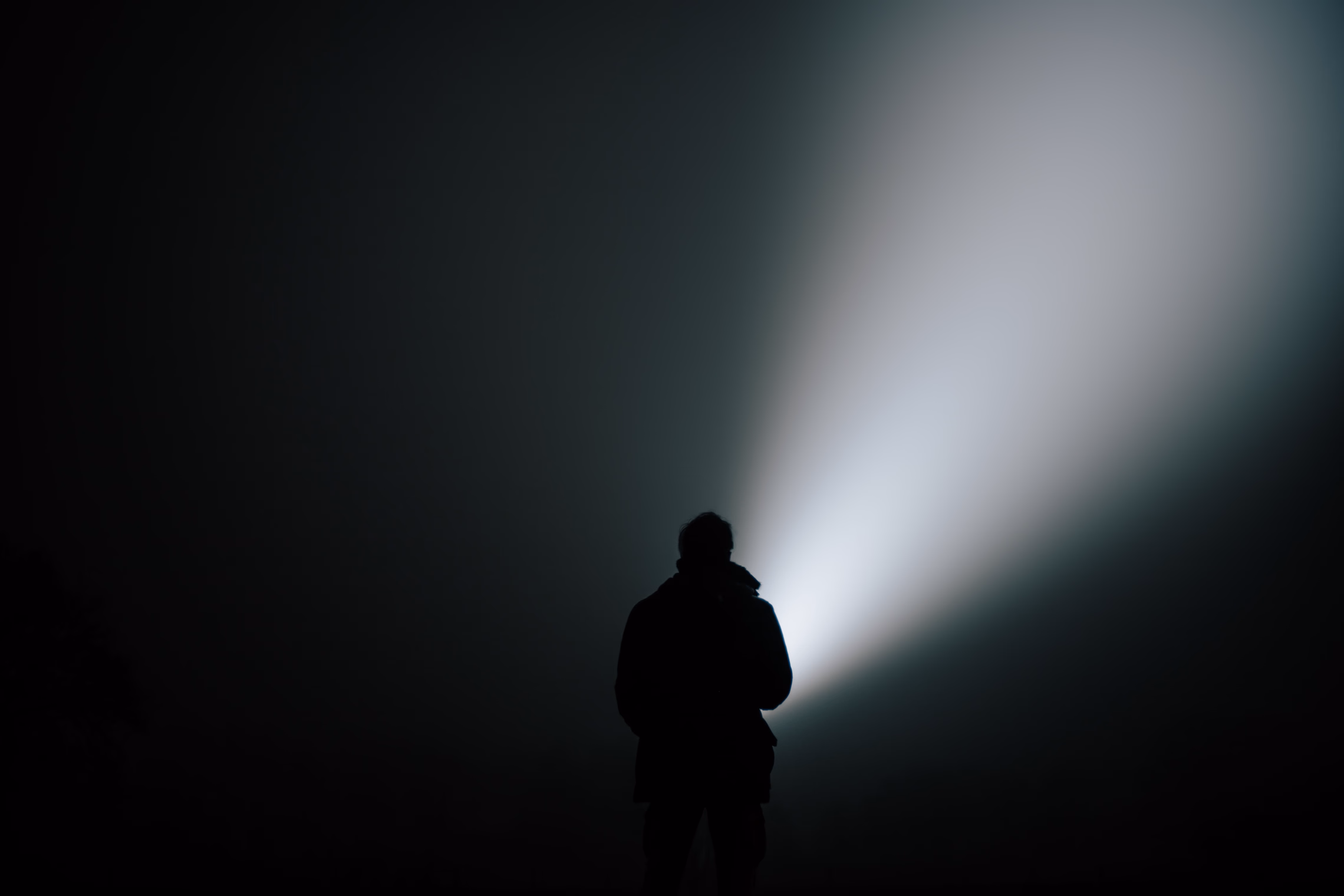 A silhouetted figure sweeping a flashlight beam through fog at night