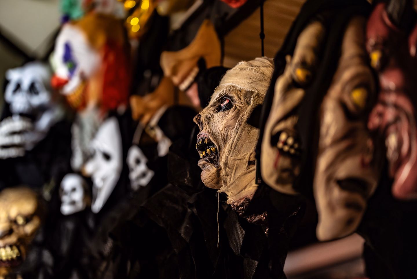 A dim row of rubber horror masks on display, including a clown, a mummy and several ghouls