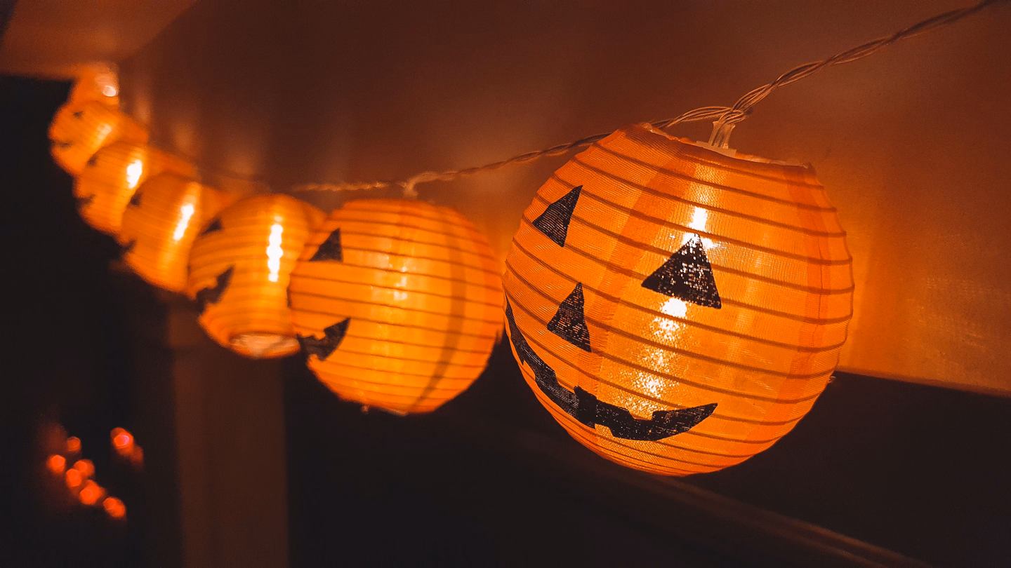 A string of orange paper jack-o'-lantern lanterns glowing along a wall in a dark room