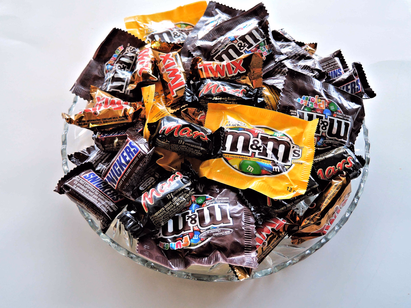 A clear glass bowl piled with individually wrapped fun-size chocolate bars and candy packs