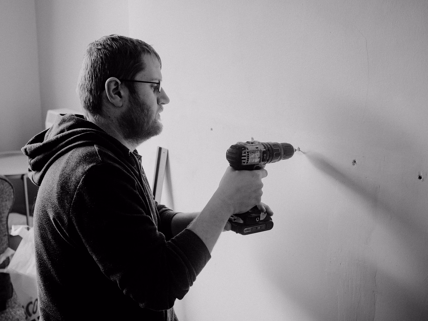 Black and white photo of a man drilling into an interior wall with a cordless drill
