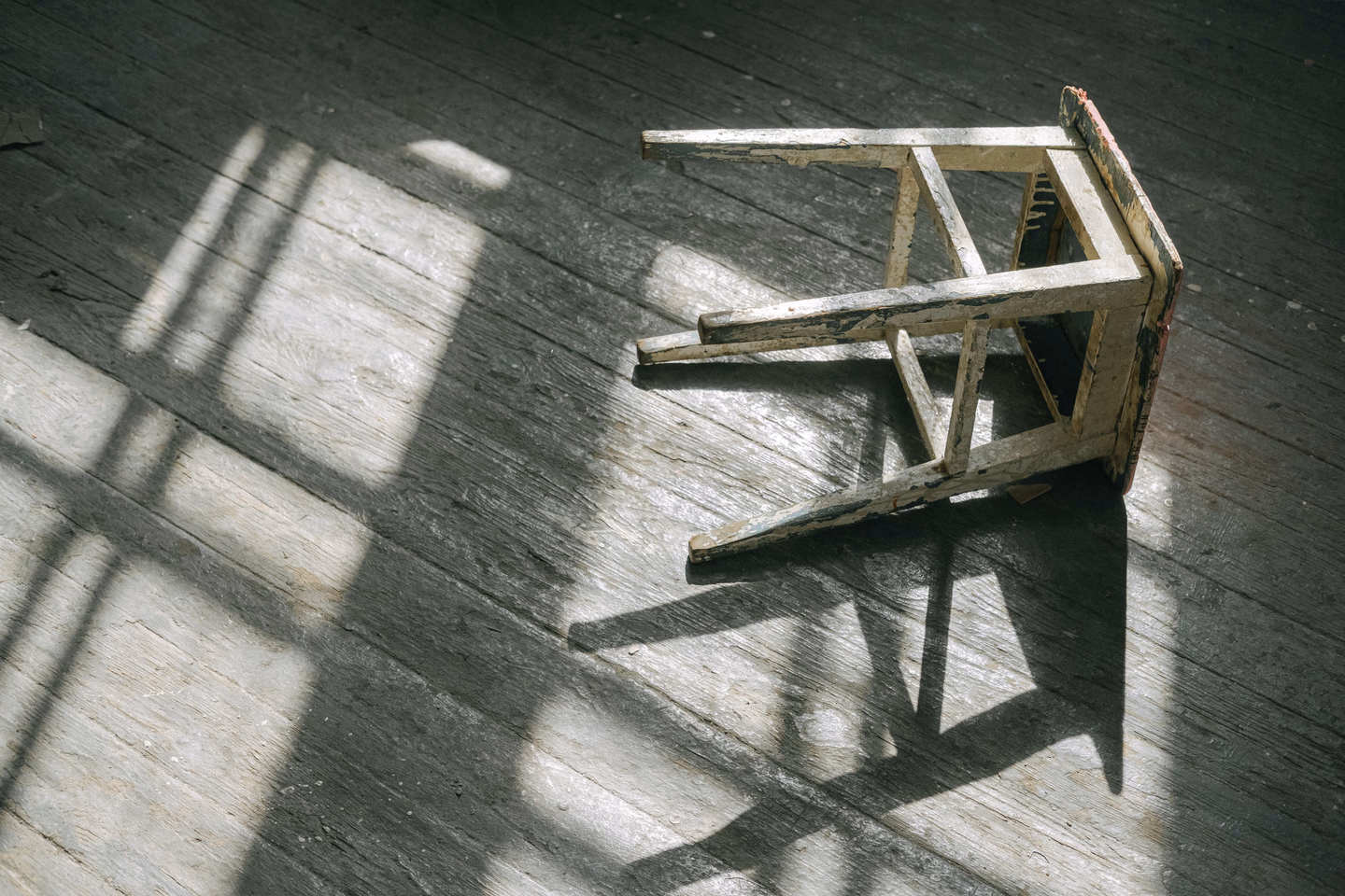 A worn wooden stool casting a long shadow across a sunlit plank floor