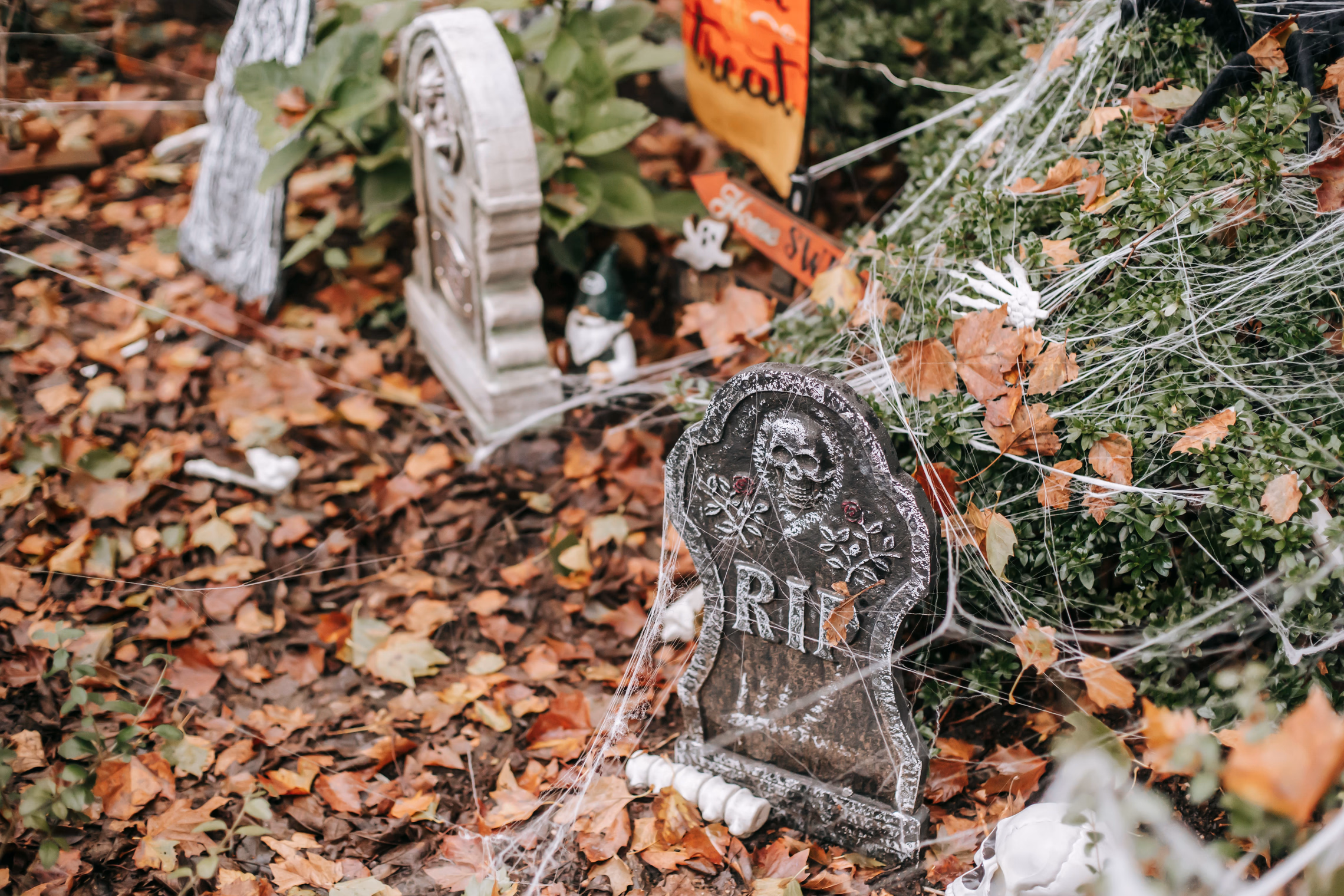 A Halloween yard display with gravestones, cobwebs, and printed signs staked into the lawn