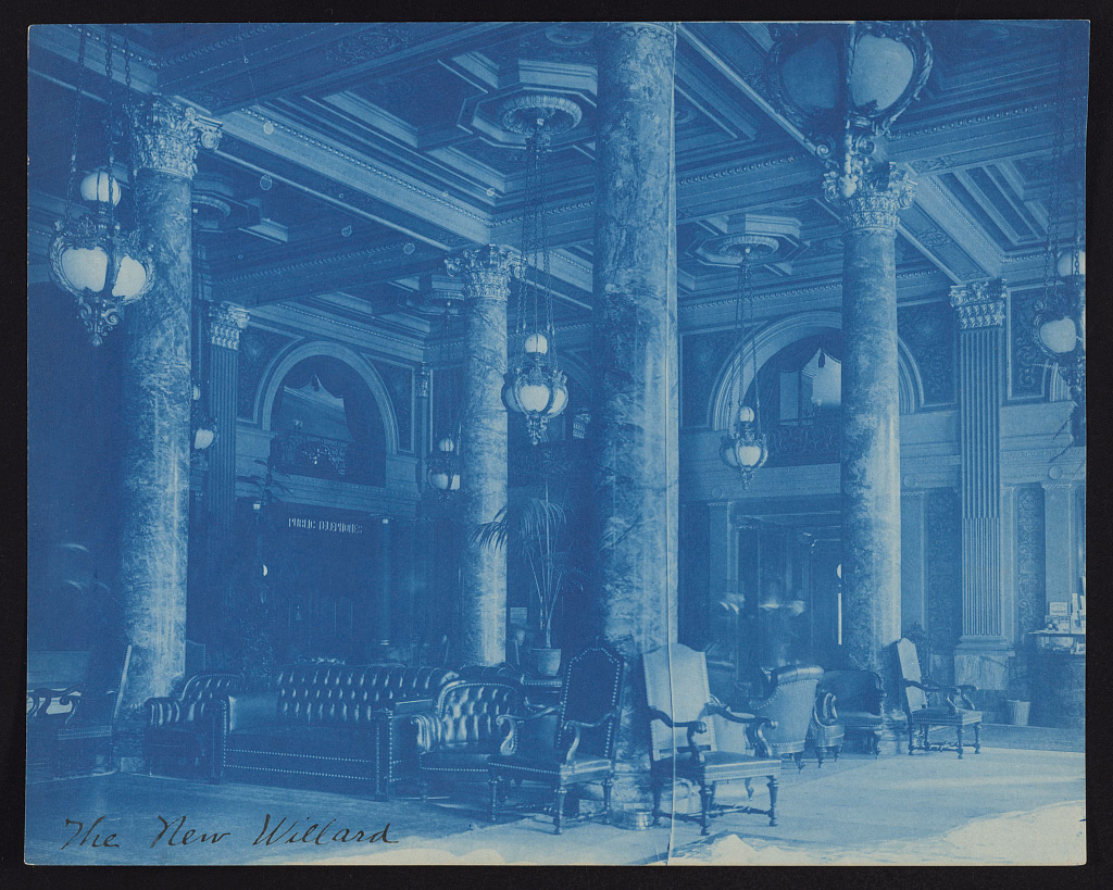 Blue cyanotype photograph of a grand hotel lobby with marble columns, a coffered ceiling, globe pendant lamps, and tufted leather sofas and carved armchairs, with 'The New Willard' handwritten along the bottom