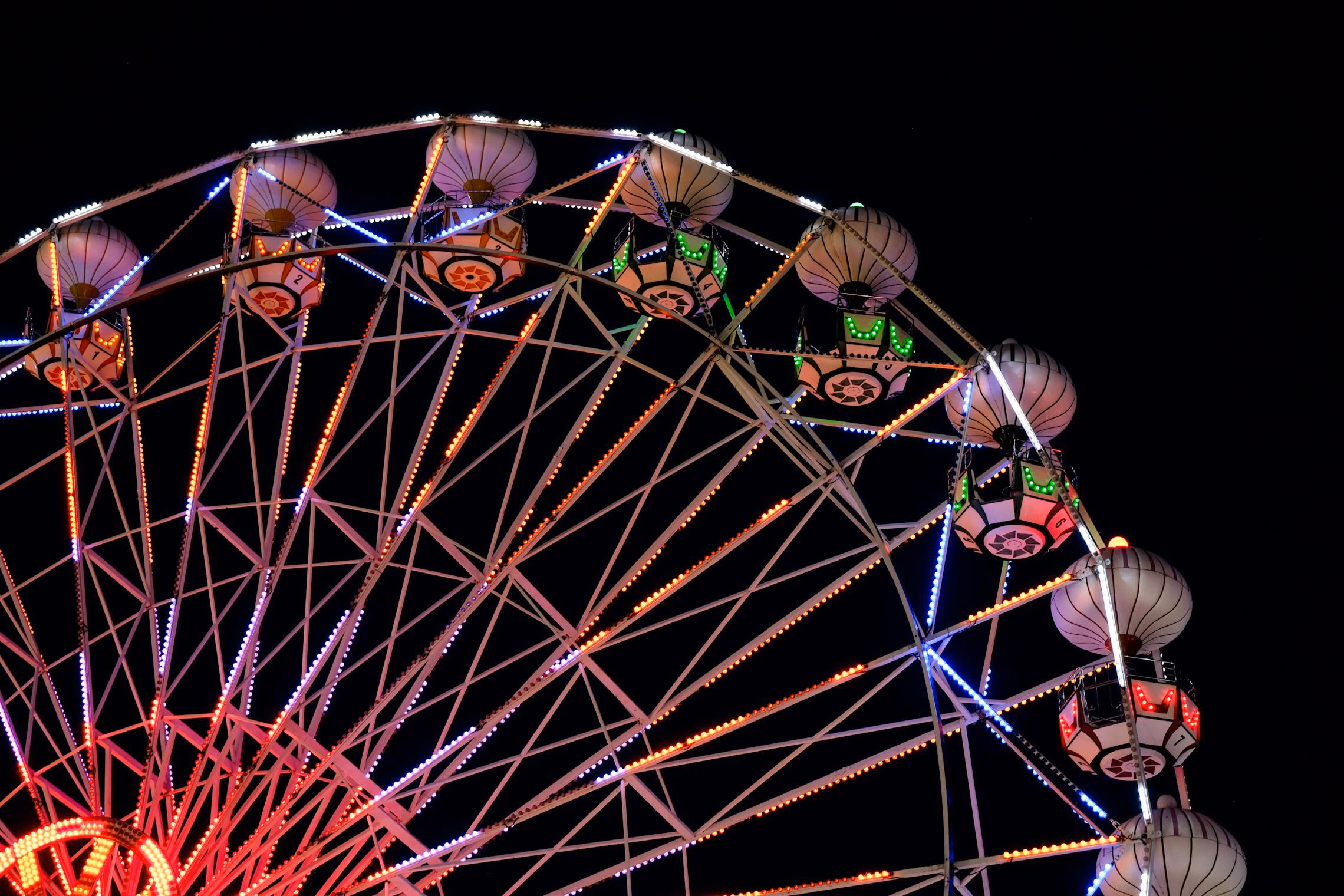 Dark carnival setup with striped fabric draping, warm string lights, fortune teller booth, and vintage carnival game stations