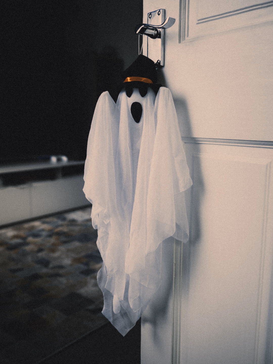 A white fabric ghost with a small black hat hanging from the handle of a white interior door