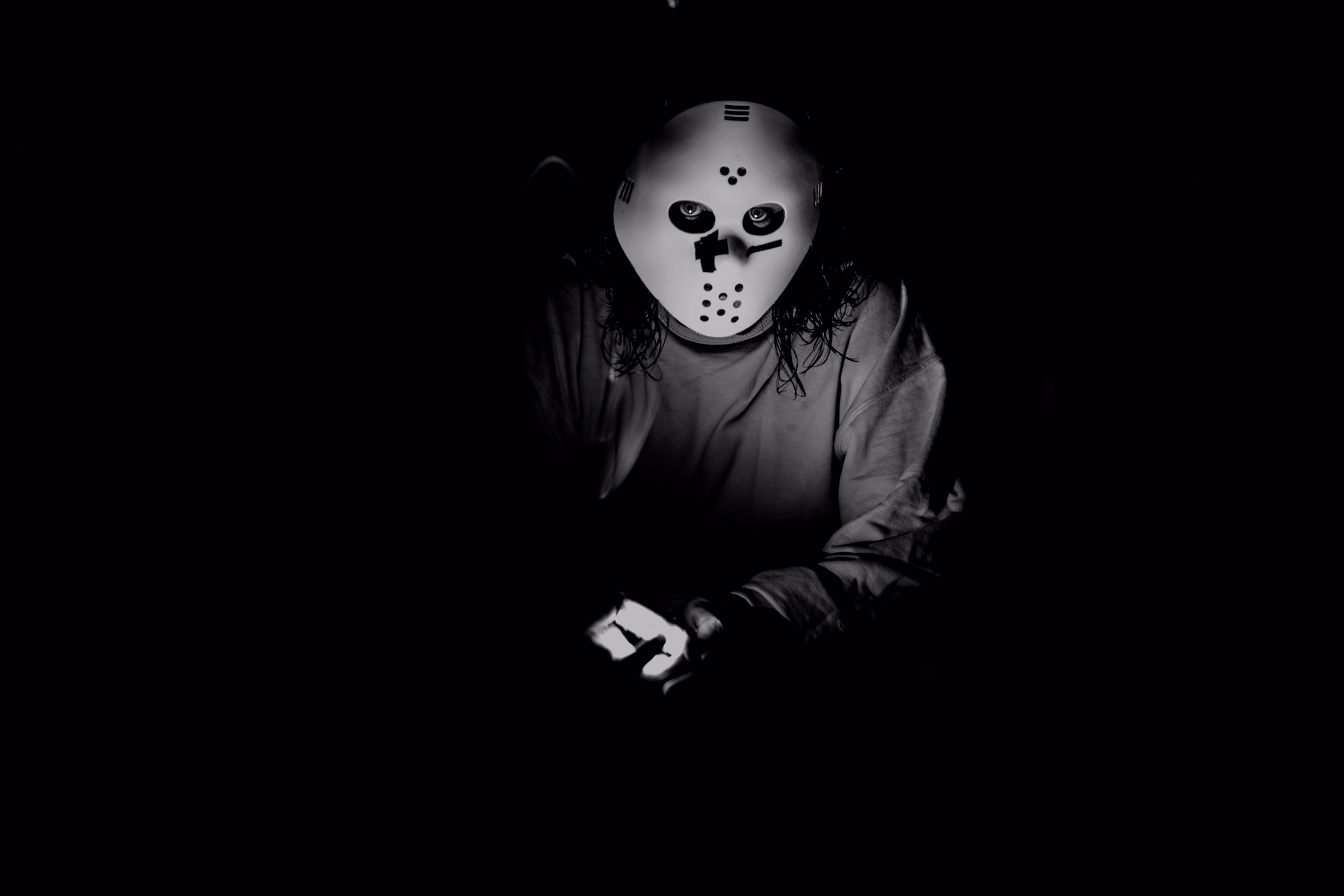 A figure in a horror mask lit from below in a dark room